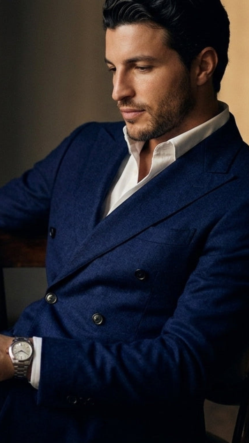 Modelo de VITTORI LUVANO sentado con traje cruzado azul marino, camisa blanca y reloj de acero